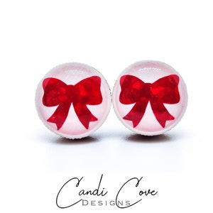 May include: A pair of red bow earrings with a white background. The earrings are made of glass and have a shiny finish.