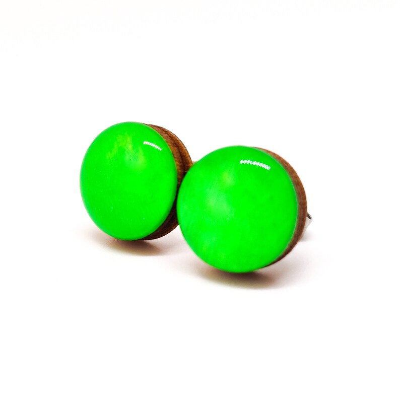 Op de afbeelding: Een paar ronde oorstekers. Elke oorbel heeft een felgroene, glanzende, cirkelvormige bovenkant op een bruine houten basis. De oorbellen worden gepresenteerd tegen een witte achtergrond.