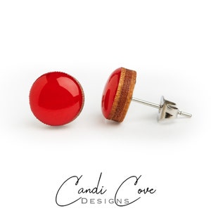 May include: A pair of red and wood stud earrings. The earrings are round and have a shiny red finish. The wood is a light brown color.