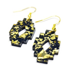 May include: A pair of black and gold earrings with a geometric design. The earrings are made of resin and have a gold glitter finish.