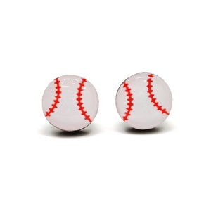 May include: A pair of baseball stud earrings. Each earring is a white sphere with red stitching, mimicking a baseball. The earrings are set against a white background.