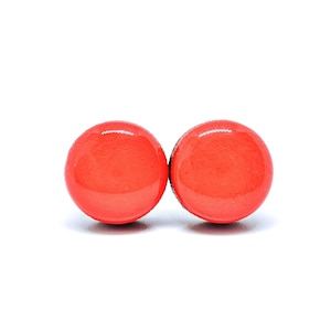 Könnte beinhalten: Ein Paar leuchtend orangefarbene runde Ohrstecker. Die Ohrringe sind aus Holz und haben eine glänzende Oberfläche.