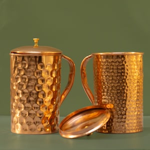May include: Two hammered copper mugs with a lid. The mugs have a textured surface and a handle. The lid is also hammered copper.