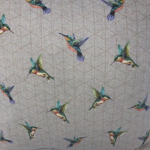 May include: A square cushion featuring a repeating pattern of hummingbirds in flight. The birds are green, orange, and purple. The background is a light tan fabric with a geometric design.