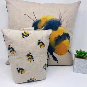 May include: Two decorative throw pillows with a watercolor design of bumblebees. The larger pillow features a single large bumblebee with yellow and black markings. The smaller pillow has a repeating pattern of smaller bumblebees.
