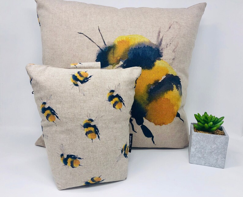 May include: Two decorative throw pillows with a watercolor design of bumblebees. The larger pillow features a single large bumblebee with yellow and black markings. The smaller pillow has a repeating pattern of smaller bumblebees.