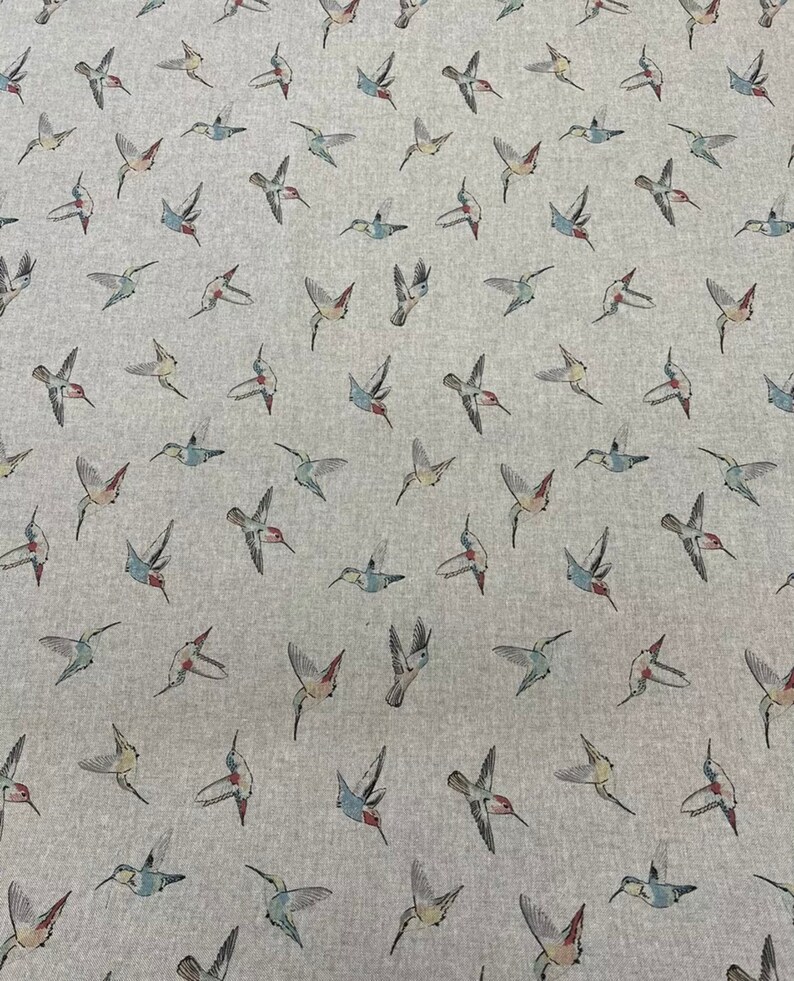 May include: Pale grey fabric with a repeating pattern of hummingbirds in flight. The birds are illustrated in shades of grey, blue, red, and green. The fabric has a soft, textured appearance, suitable for various sewing projects.