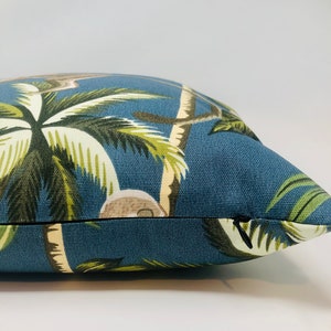May include: A blue throw pillow with a tropical print featuring palm trees and coconuts. The pillow has a zipper closure.