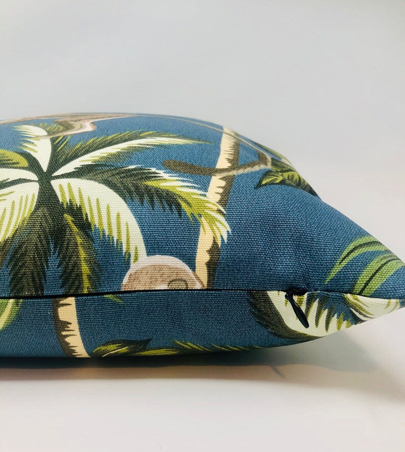 May include: A blue throw pillow with a tropical print featuring palm trees and coconuts. The pillow has a zipper closure.