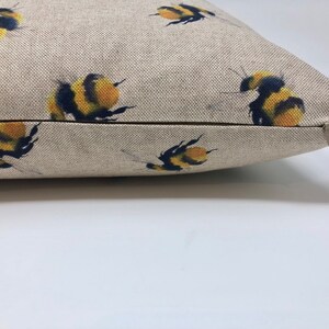 May include: A beige linen pillow with a zipper closure features a repeating pattern of yellow and black bumblebees.