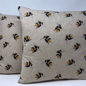 May include: Two beige linen throw pillows with a repeating pattern of yellow and black bumblebees.