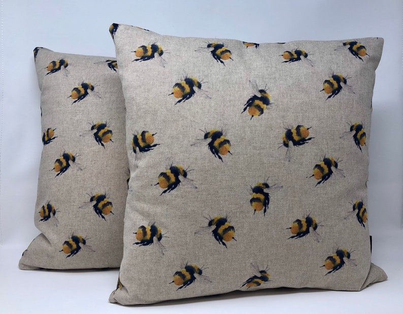 May include: Two beige linen throw pillows with a repeating pattern of yellow and black bumblebees.