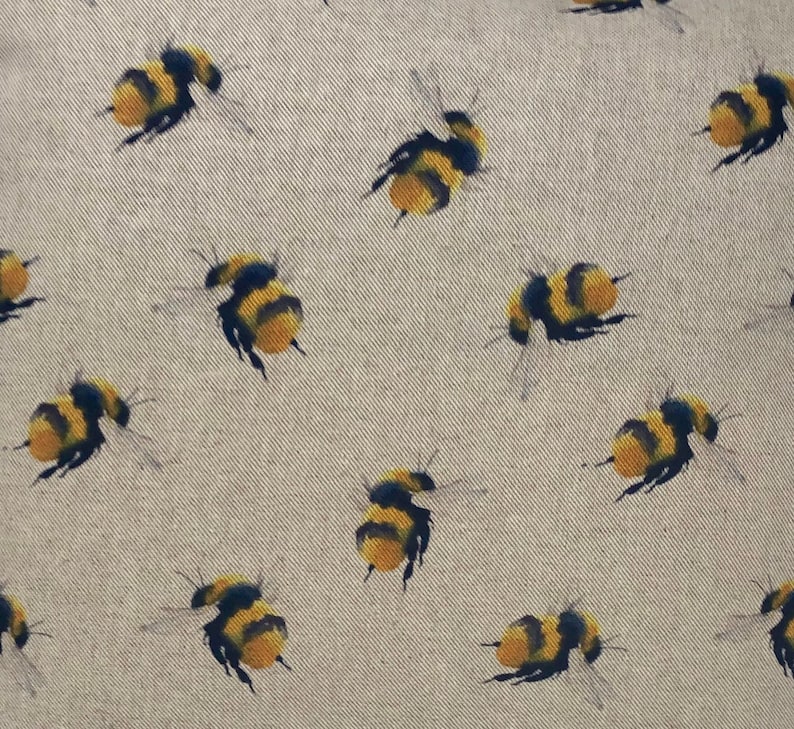 May include: A beige fabric with a repeating pattern of yellow and black bumblebees. The bees are flying in different directions.