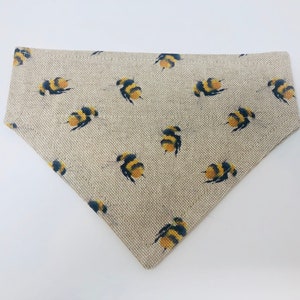 May include: A beige linen dog bandana with a repeating pattern of yellow and black bumblebees.