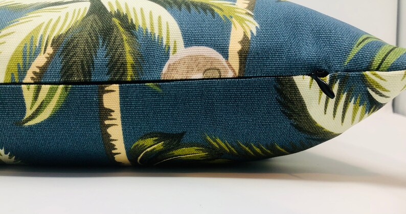 May include: A blue throw pillow with a tropical palm tree print. The pillow has a zipper closure.