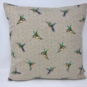 May include: Square cushion featuring a repeating pattern of hummingbirds. The birds are depicted in green, blue, and red against a neutral background with a geometric design. The cushion is square in shape.