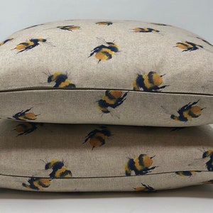 May include: Two beige linen pillow covers with a repeating pattern of yellow and black bumblebees. The pillow covers have a zipper closure.