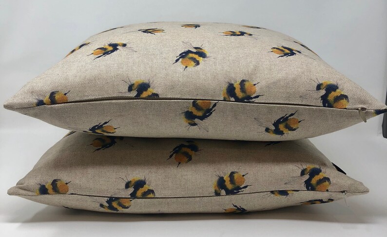 May include: Two beige linen pillow covers with a repeating pattern of yellow and black bumblebees. The pillow covers have a zipper closure.