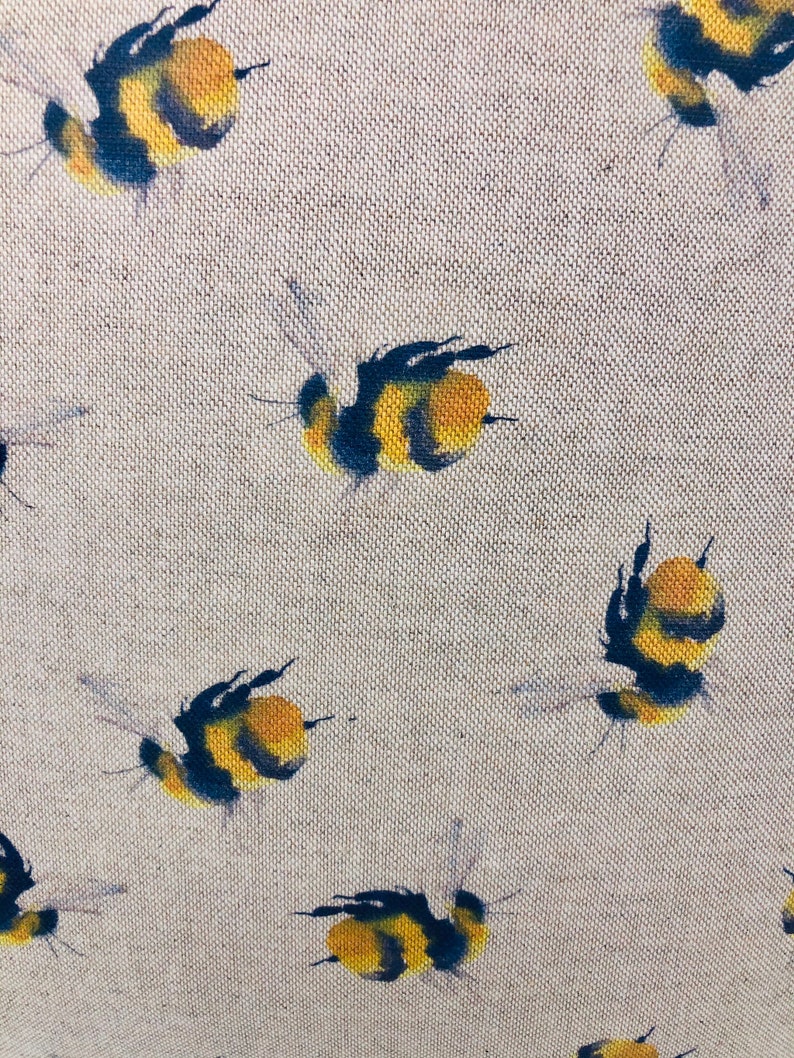 May include: A beige fabric with a repeating pattern of black and yellow bumblebees. The bees are painted in a watercolor style and are flying in different directions.