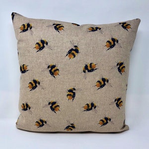 May include: A beige linen cushion cover with a repeating pattern of yellow and black bumblebees.