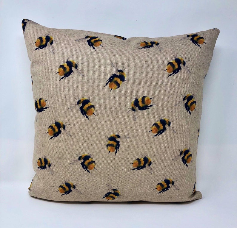 May include: A beige linen cushion cover with a repeating pattern of yellow and black bumblebees.