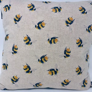 May include: A beige linen pillow cover with a repeating pattern of yellow and black bumblebees. The pillow cover is a soft, natural fabric with a subtle texture.