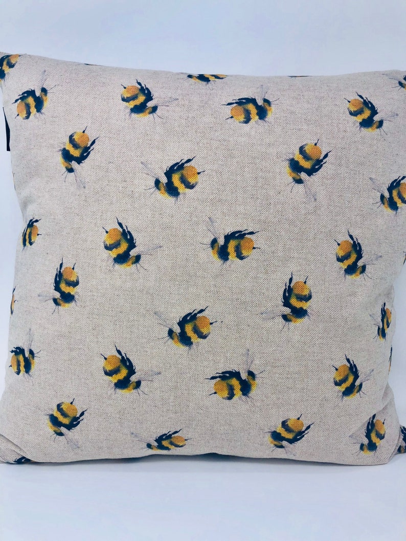 May include: A beige linen pillow cover with a repeating pattern of yellow and black bumblebees. The pillow cover is a soft, natural fabric with a subtle texture.