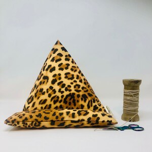 May include: A triangular leopard print cushion with a brown fabric base. The cushion is designed to prop up a tablet or book.