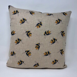 May include: A beige linen pillow cover with a repeating pattern of yellow and black bumblebees.