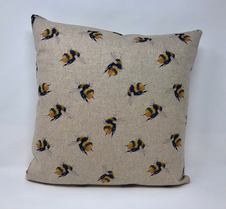 May include: A beige linen pillow cover with a repeating pattern of yellow and black bumblebees.