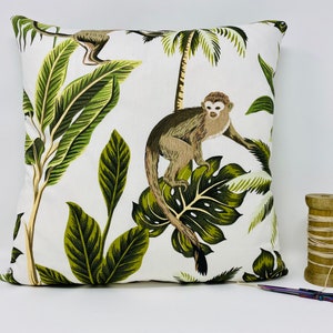 May include: White throw pillow with a tropical print featuring monkeys and palm leaves. The pillow has a green, brown, and white color scheme.