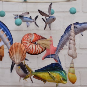 May include: A colorful mobile with a variety of sea creatures, including a marlin, a dolphin, a nautilus shell, a flying fish, and a starfish. The mobile is made of felt and fabric and is perfect for a nursery or child's room.