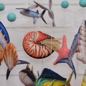 May include: A colorful mobile with various sea creatures, including a nautilus shell, a starfish, a marlin, a flying fish, and a seashell. The mobile is made of felt and is perfect for a child's room.