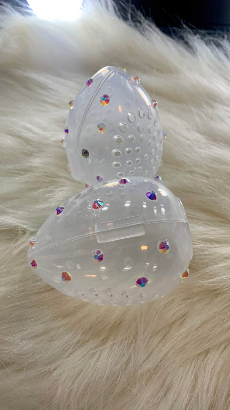 May include: Two clear plastic egg-shaped containers with a pattern of small holes and iridescent rhinestones.