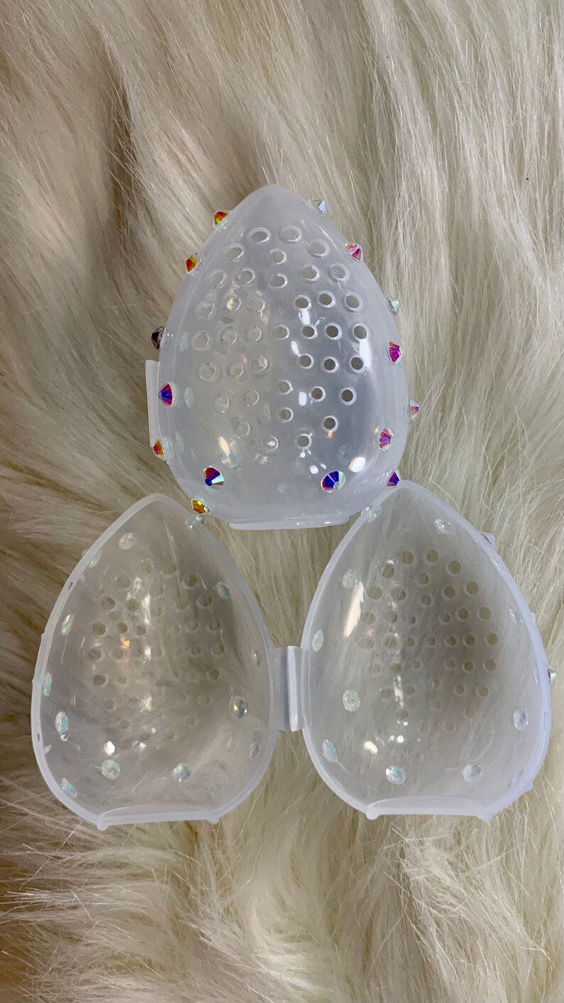 May include: Three clear plastic makeup sponge holders with a mesh design and rhinestones. The holders are shaped like a teardrop.