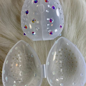 May include: A clear plastic makeup sponge holder with a decorative design of iridescent rhinestones. The holder is divided into two halves, each with a honeycomb-like pattern.