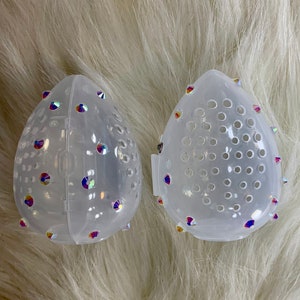 May include: Two clear plastic containers with a diamond-shaped design. The containers have a small hole pattern and are decorated with iridescent rhinestones.