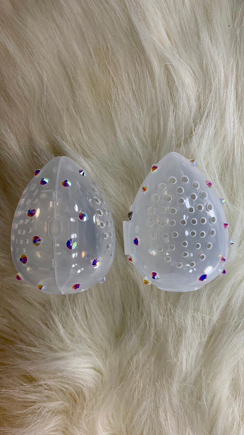 May include: Two clear plastic containers with a diamond-shaped design. The containers have a small hole pattern and are decorated with iridescent rhinestones.