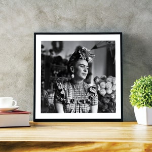 May include: Black and white portrait photograph of Frida Kahlo wearing a flower crown and a plaid dress. She is looking to the right of the frame.