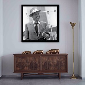 May include: A black and white photograph of a man in a suit and hat, holding a cigarette. The photo is framed and hanging on a white wall above a wooden cabinet with three bronze hippopotamus figurines on top.