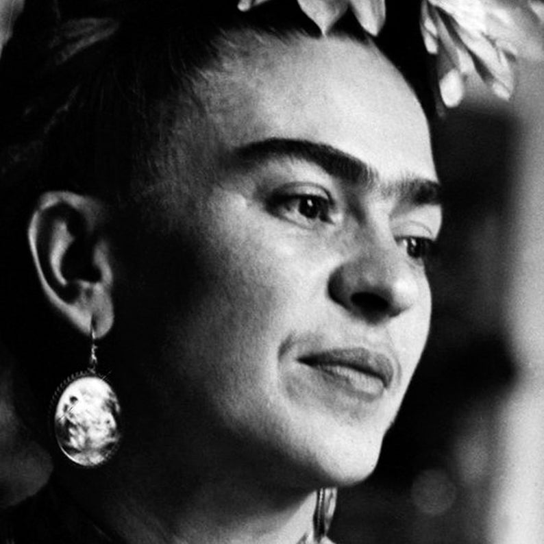 May include: Black and white portrait of a woman with a unibrow, wearing a flower crown and large, round earrings. She is looking off to the side with a thoughtful expression.