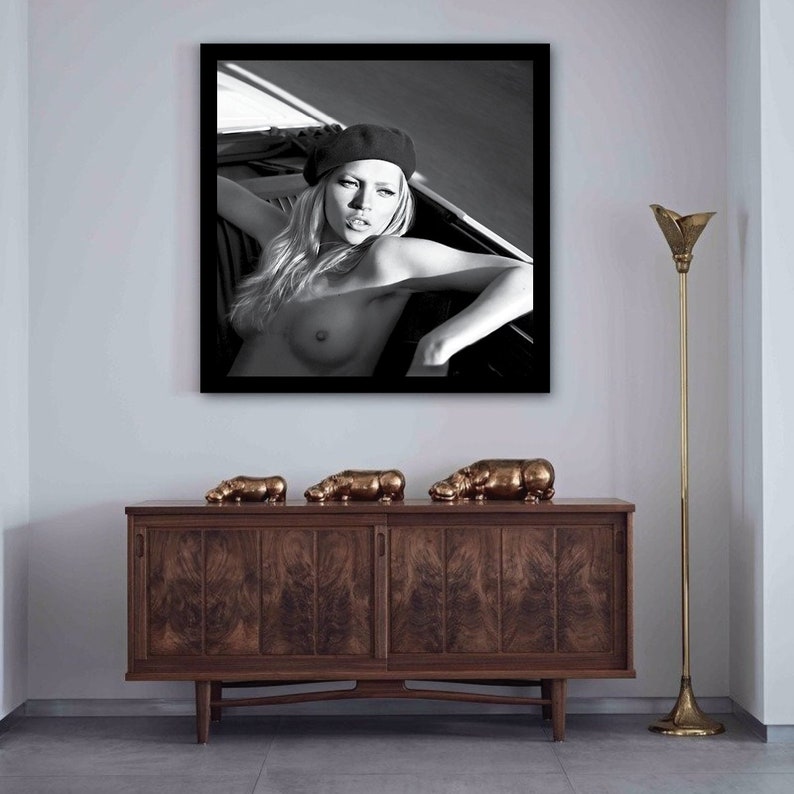 Peut inclure: Une photographie en noir et blanc d'une femme portant un b&eacute;ret noir et allong&eacute;e sur un lit. La photo est encadr&eacute;e d'un cadre noir et est accroch&eacute;e &agrave; un mur blanc.
