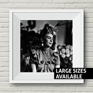 May include: Black and white portrait photograph of Frida Kahlo wearing a flower crown and a plaid dress. The image is framed in a white frame with the text "LARGE SIZES AVAILABLE" at the bottom.