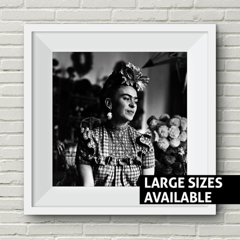 May include: Black and white portrait photograph of Frida Kahlo wearing a flower crown and a plaid dress. The image is framed in a white frame with the text "LARGE SIZES AVAILABLE" at the bottom.