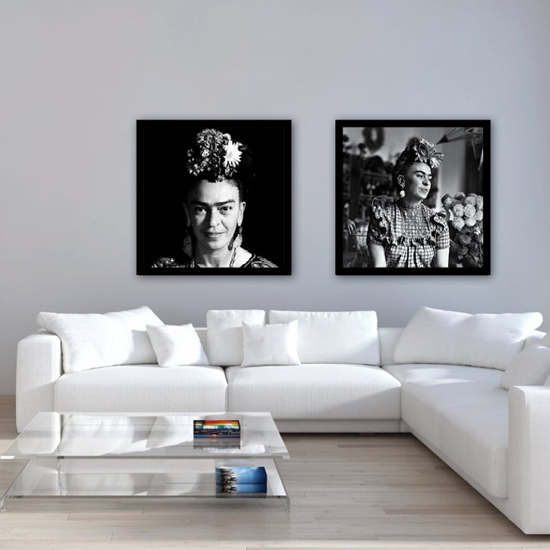 May include: Two black and white framed photographs of Frida Kahlo. The first photo shows Frida Kahlo looking directly at the camera with flowers in her hair. The second photo shows Frida Kahlo sitting in a chair with flowers in her hair and a floral background.