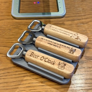 Op de afbeelding: Vier houten flessenopeners met metalen flessenopenerkoppen. De openers hebben gegraveerde spreuken, waaronder "The best way to spread Christmas cheer is singing loud and drinking beer", "You're not drunk if you can lie on the floor without holding on" en "Beer O'Clock".