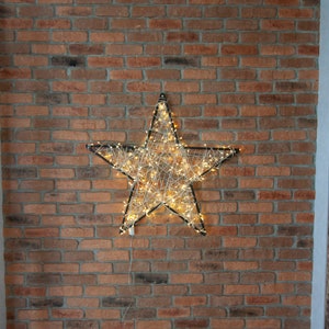 以下が含まれることがあります： 白い紐状の電球が全体に張り巡らされた、大きな黒い金属製の星型の照明器具。星はレンガの壁に取り付けられている。