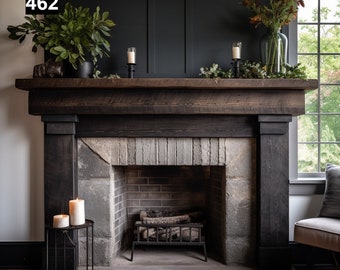 Op de afbeelding: Een rustieke open haard met een donkere houten mantel en een stenen haard. De mantel is versierd met groen, kaarsen en een vaas met bloemen. Een kleine metalen bijzettafel heeft twee brandende kaarsen. De muur achter de mantel is donker.