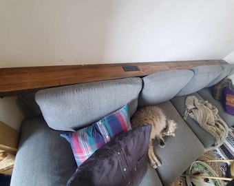 Behind the couch shelf with power outlet