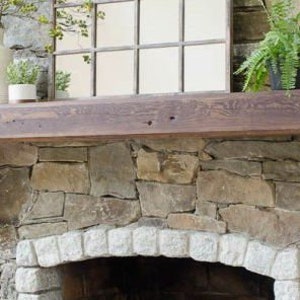 May include: A rustic wooden mantel shelf with a stone fireplace below. The mantel is supported by two wooden brackets. The fireplace has a stone archway and a black metal grate.
